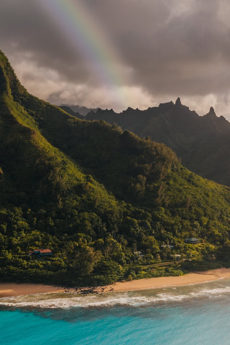 Idyllic view of lush mountains, vibrant sea, and a rainbow over a Hawaiian beach.
